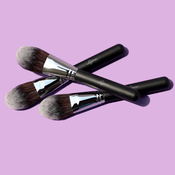 Luscious Cosmetics all-over powder brushes with black handles and silver ferrules on a purple background.