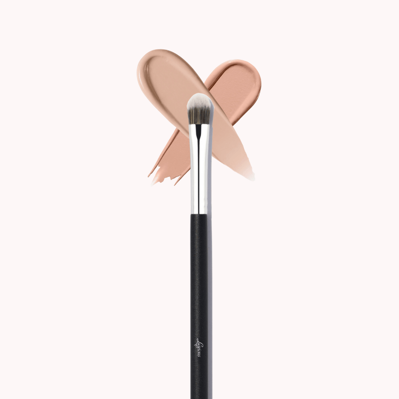 Luscious Cosmetics makeup brush with a pink bow detail and beige color swatch on a white background.