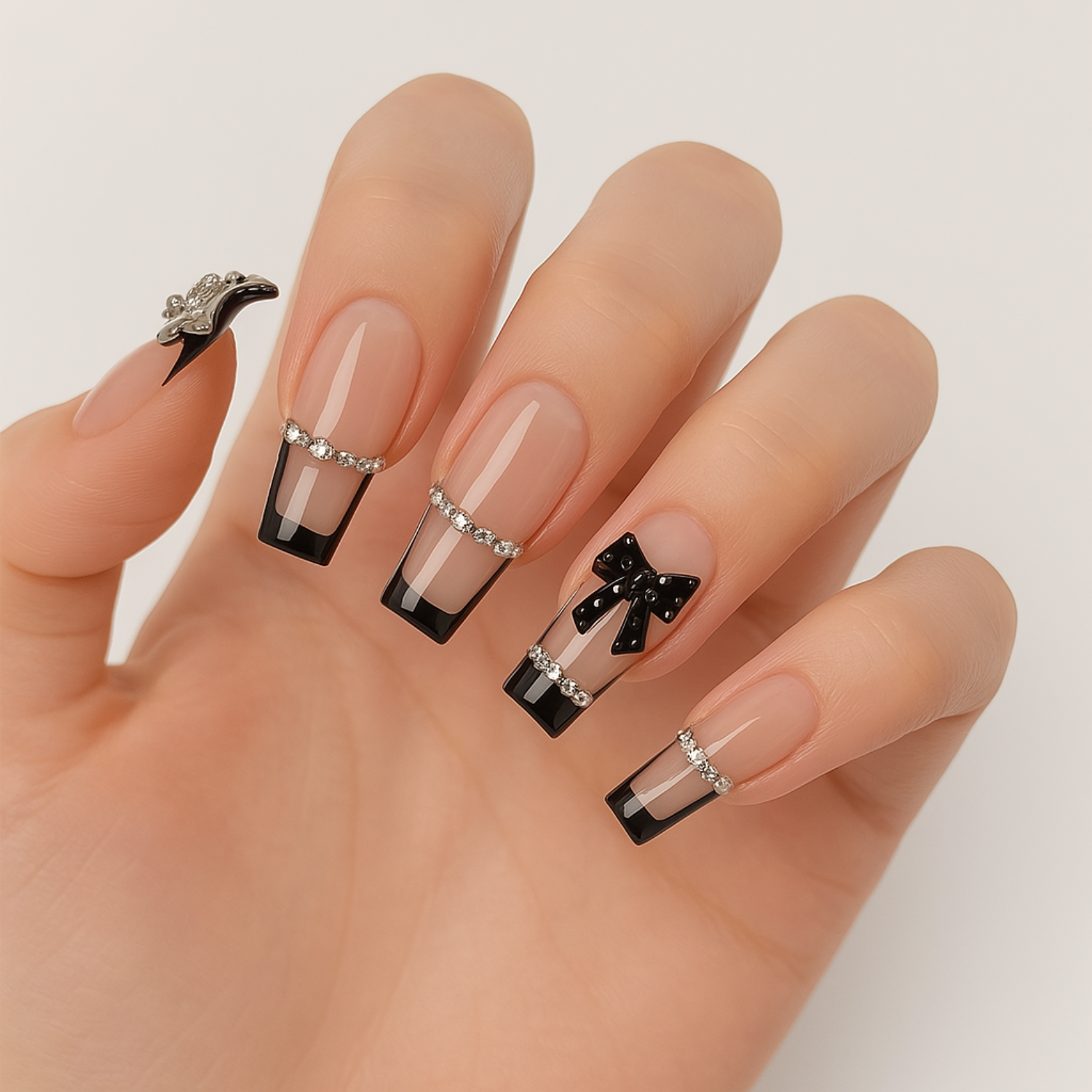 Hand wearing Luscious Cosmetics press-on nails with glossy finish, black tips, and silver decorative accents including bows and rhinestones.