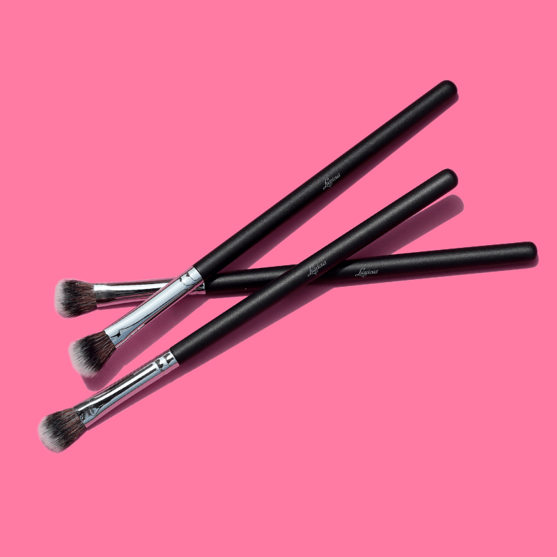 Luscious Cosmetics eyeshadow packer brushes displayed on a pink background.
