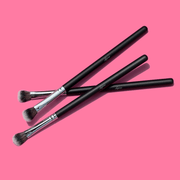 Luscious Cosmetics eyeshadow packer brushes displayed on a pink background.