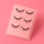 Three pairs of Luscious Cosmetics false eyelashes displayed on a pink foam board, featuring wispy lengths for a soft, wide-eyed look.