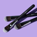 Luscious Cosmetics foundation makeup brush with black handle and silver ferrule on a purple background.
