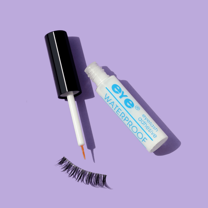Luscious Cosmetics eyelash adhesive with applicator and false eyelashes on a purple background.