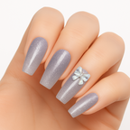 A hand wearing long, glossy lilac press-on nails by Luscious Cosmetics, featuring a floral design on the ring finger.