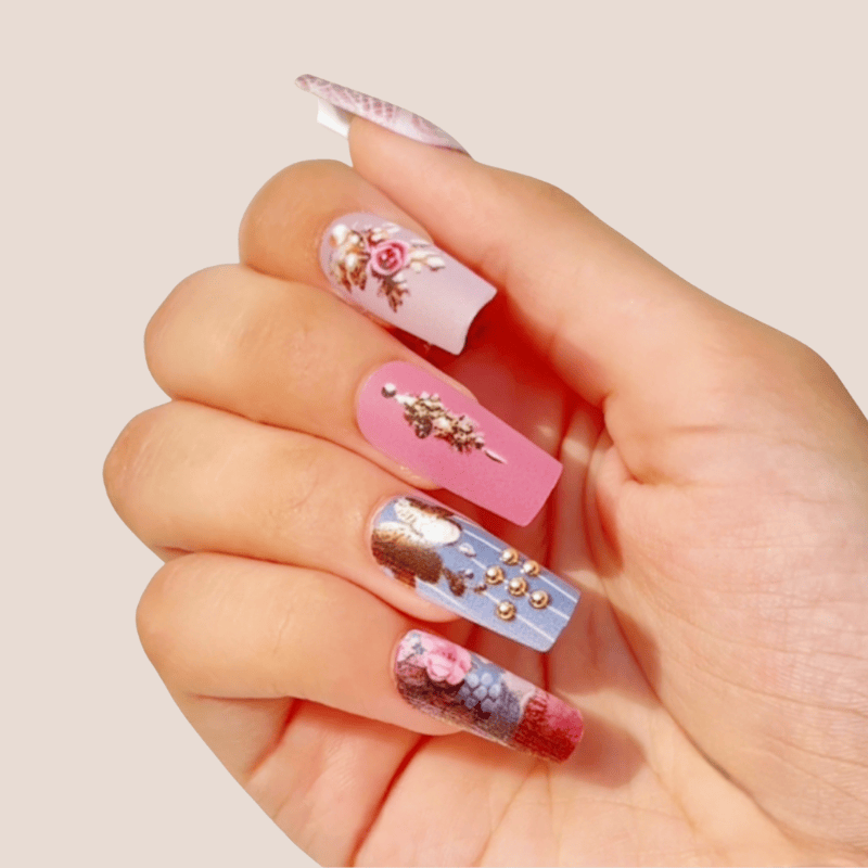 Hand with intricately designed floral nail art and gold accents by Luscious Cosmetics on a beige background.