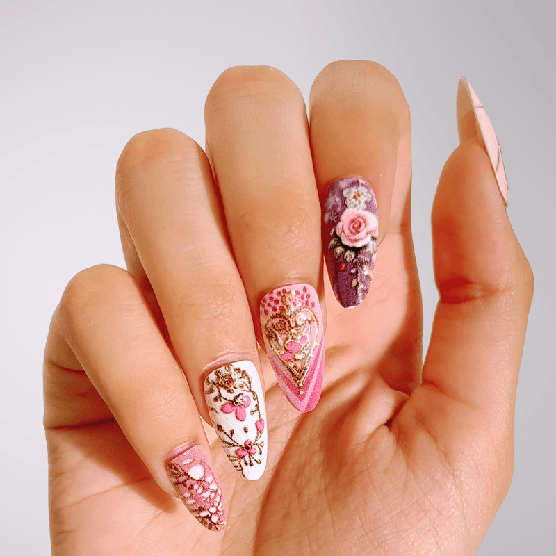 Hand with intricately designed floral and heart nail art by Luscious Cosmetics on a neutral background.