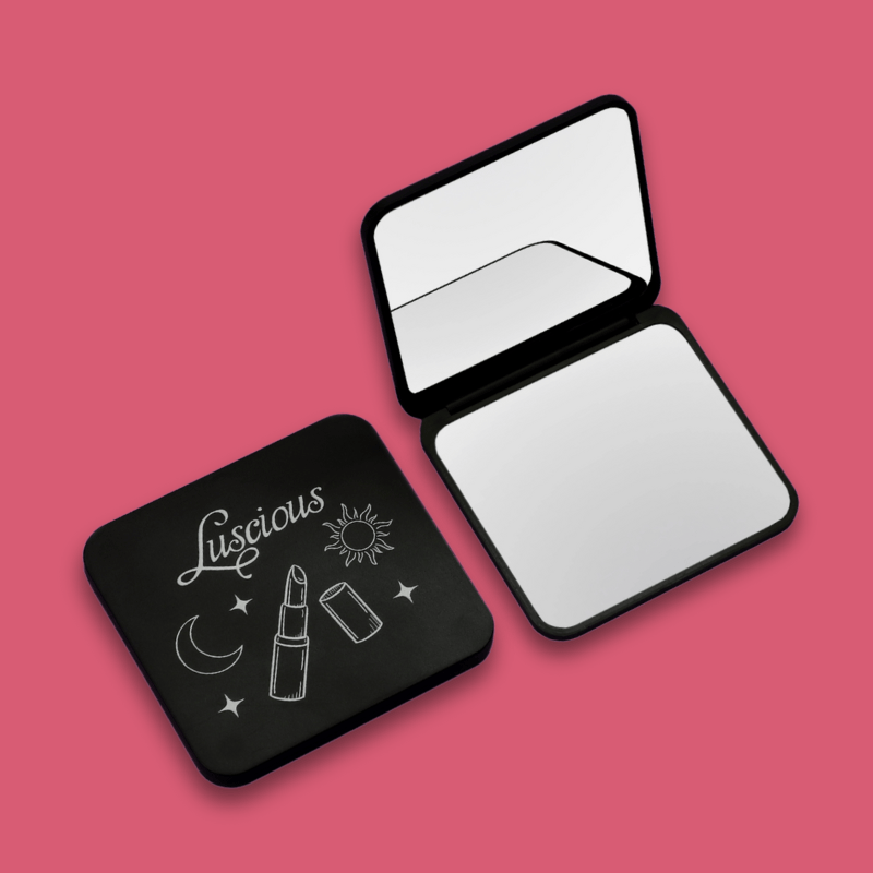 Luscious Cosmetics on-the-go compact makeup mirror with black finish on a pink background.