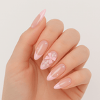 A hand wearing glossy pink press-on nails by Luscious Cosmetics, decorated with a French-style design and pearl bow detail.