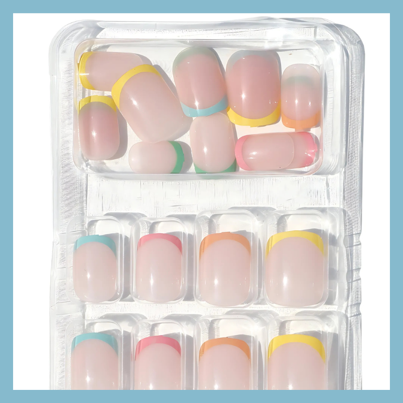 Clear plastic tray displaying Luscious Cosmetics press-on nails with pastel rainbow-colored tips.