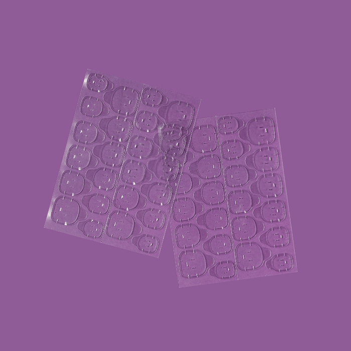 Two sheets of clear adhesive tabs by Luscious Cosmetics on a purple background.